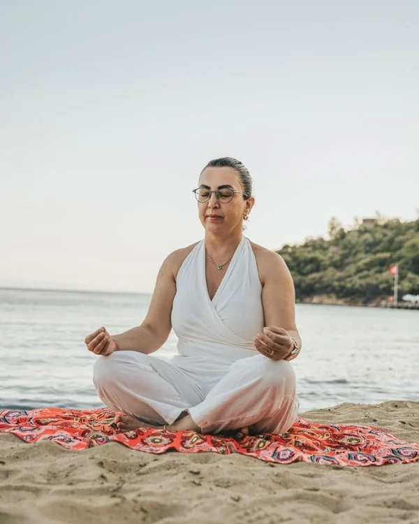 Deniz kıyısında, sabah ışığında meditasyon yaparken oturan Elvan